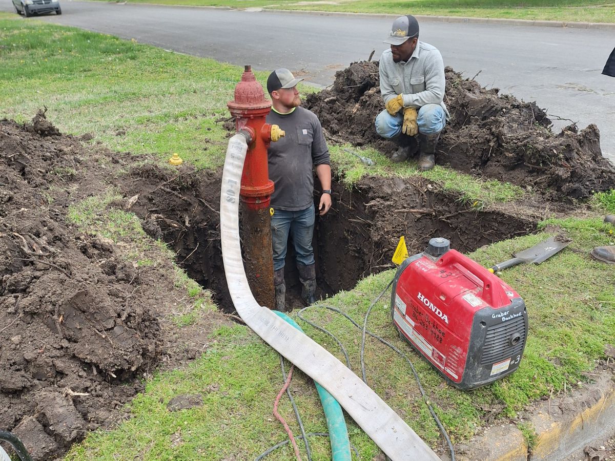 draining a hydrant before it is replaced, large hole dug all around it, equipment, men working