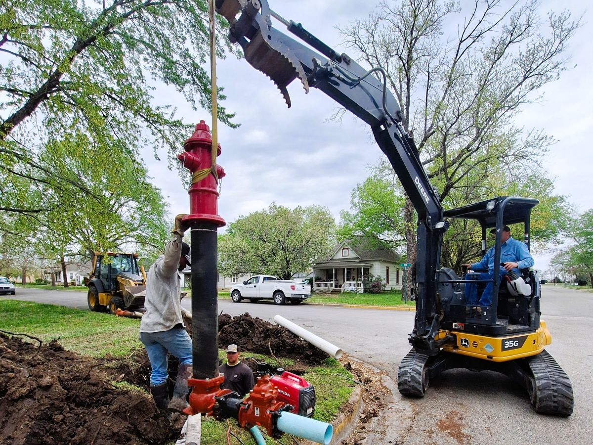 bringing the new hydrant and valve over to place in the hole, men and machinery