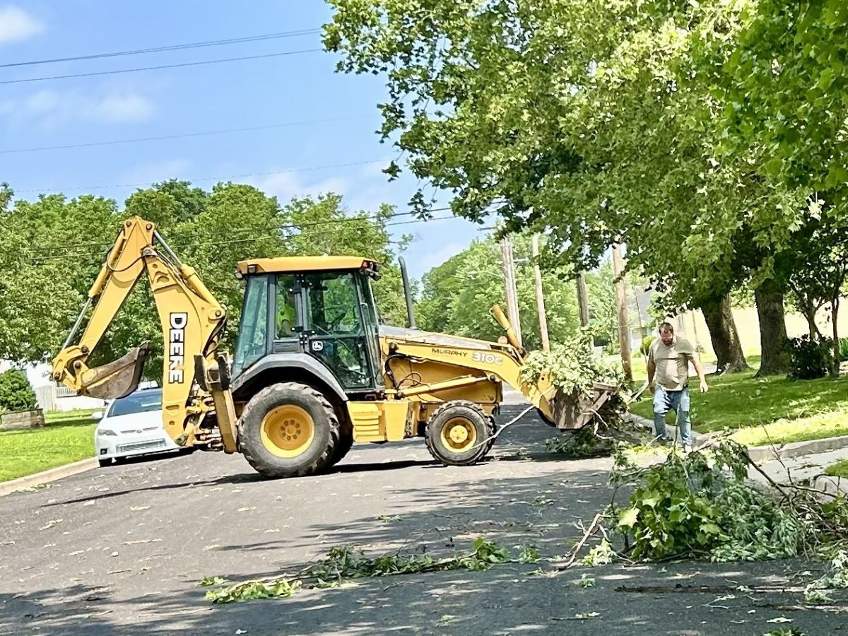 backhoe cleaning up downed branches in the middle of the road