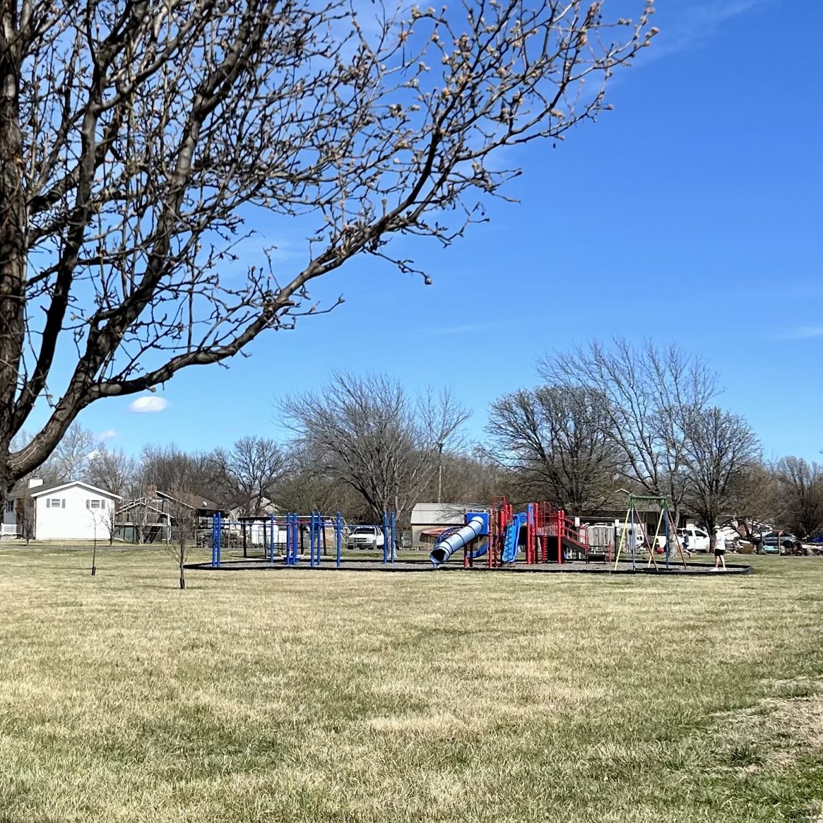 open area with grass surrounding playground equipment and a sidewalk beside it