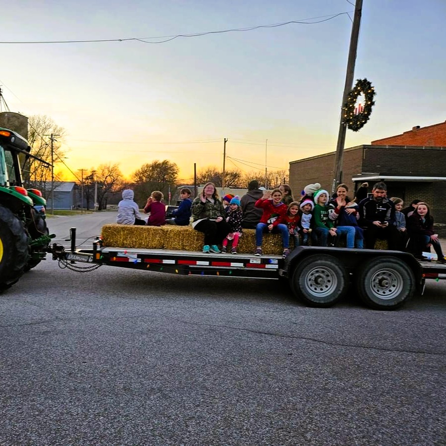 Folks sitting on hay bales on a trailer being pulled by a tractor