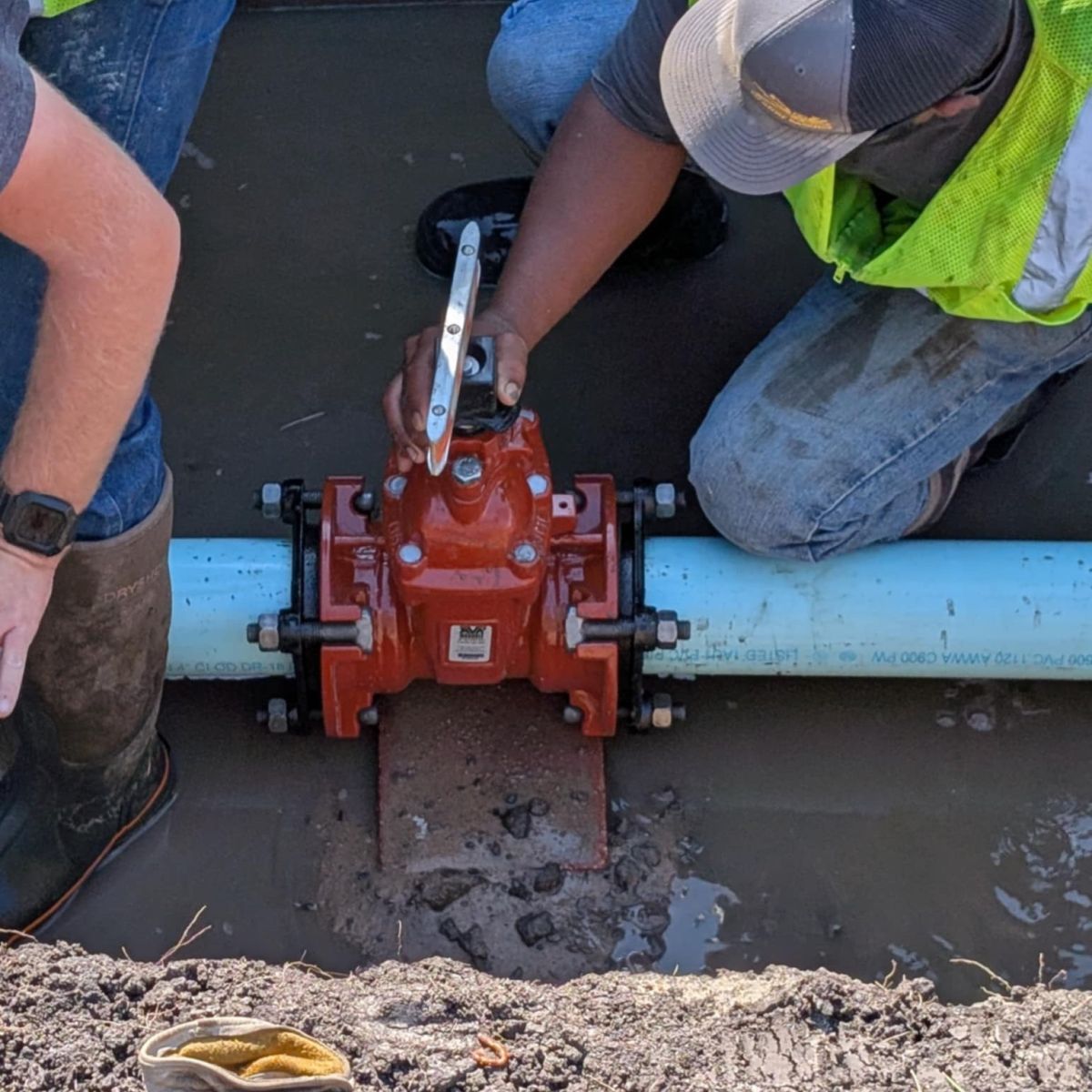 in a wet hole, two guys repair a water pipe