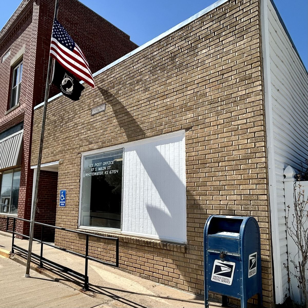 flags flying out front of the post office, a mailbox is outside