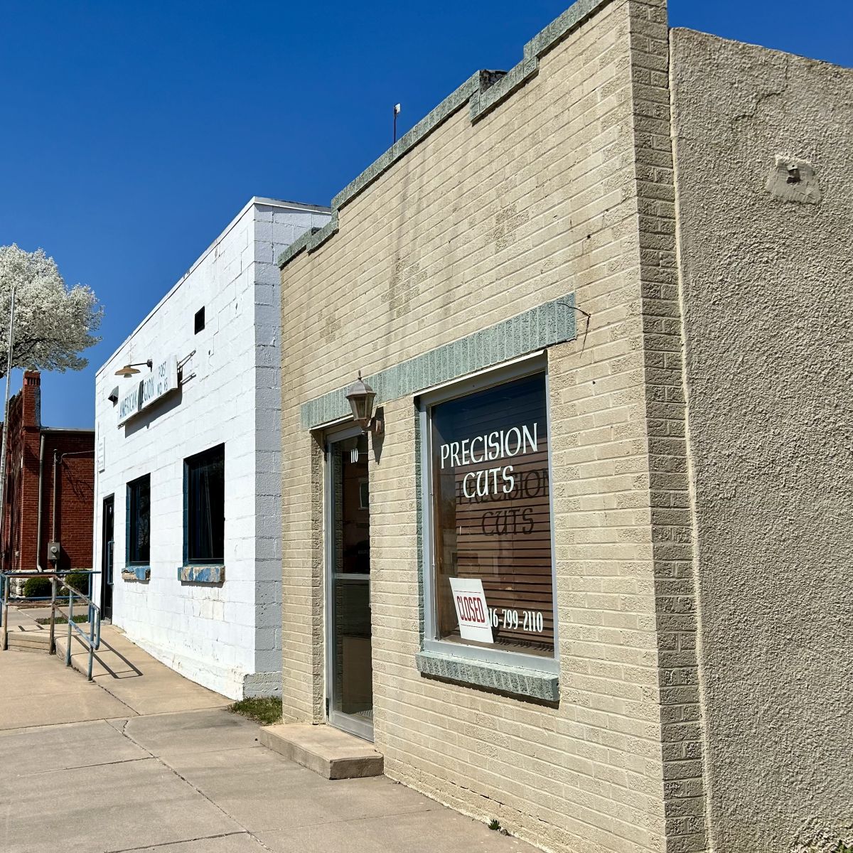 one white building home to the American Legion and a smaller brown building home to a hair salon