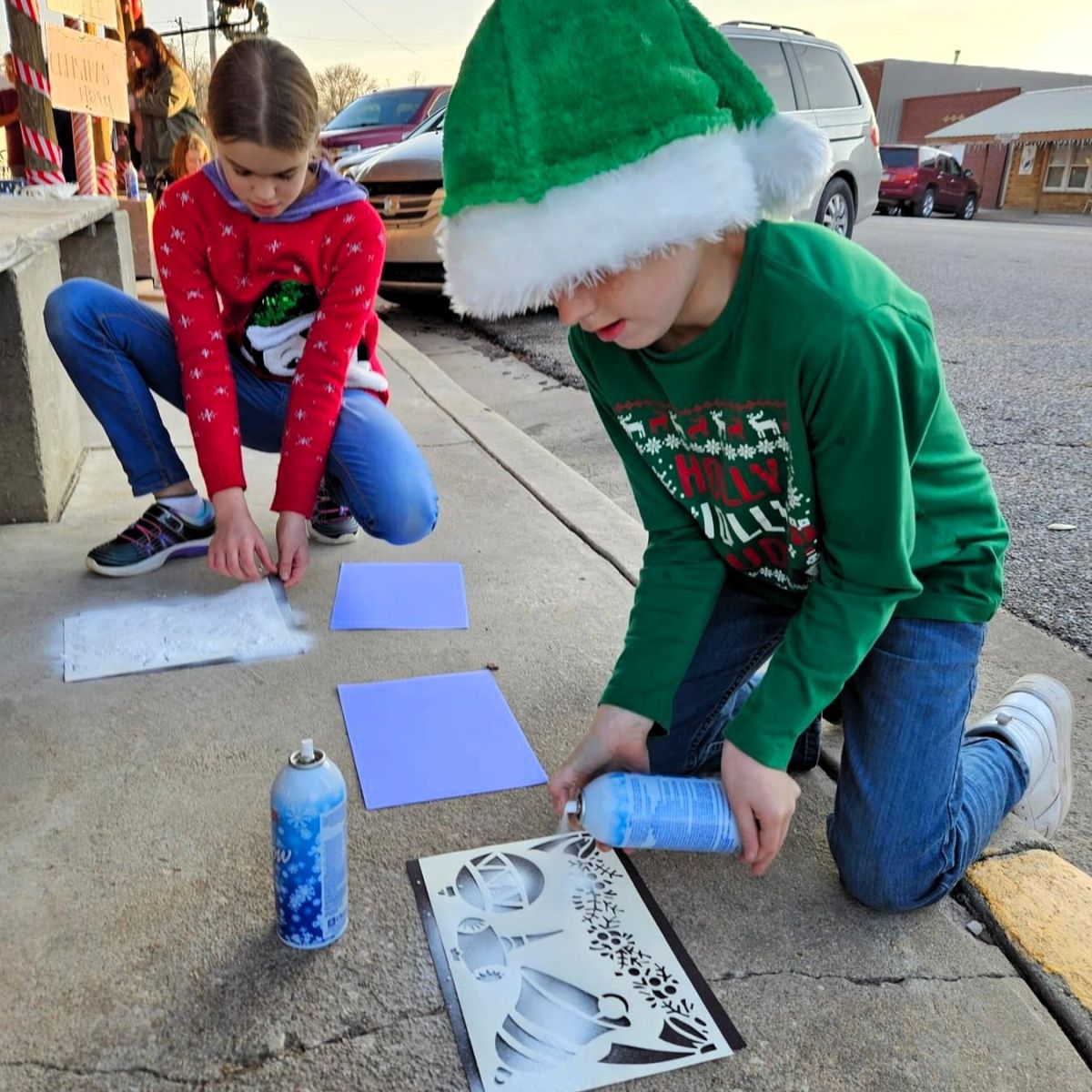 two children with elf hats doing seasonal crafts on the sidewalk