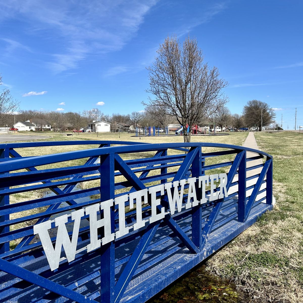 blue metal walking bridge with white lettering a playground is in the background