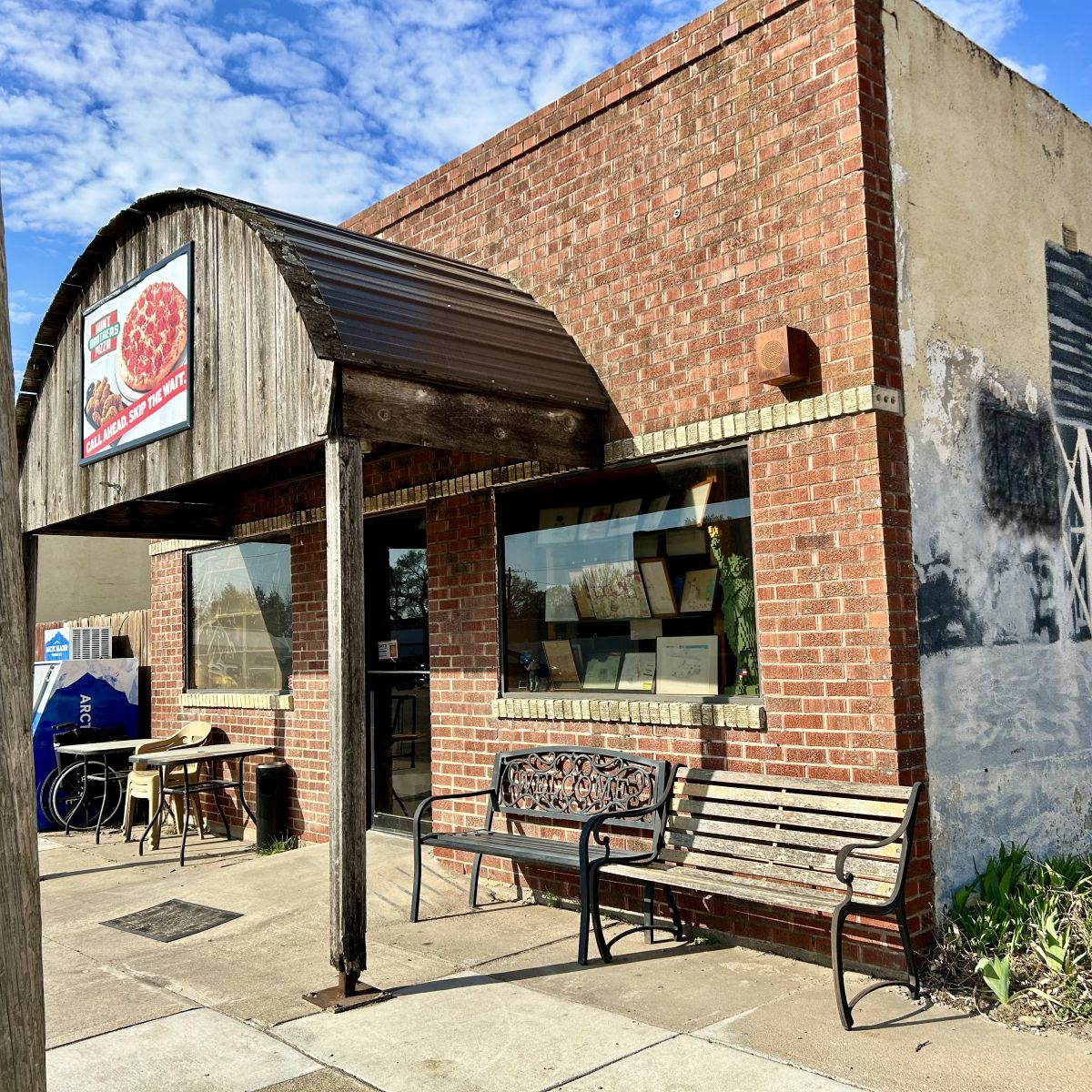 Small building with a wooden awning home to the pizza place, ice machine out front