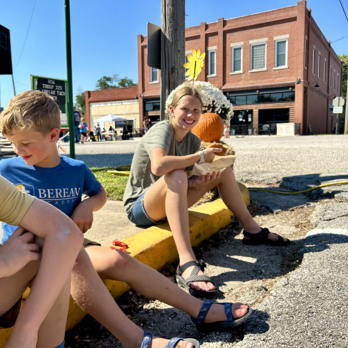 children sitting on the curb eating their festival foods