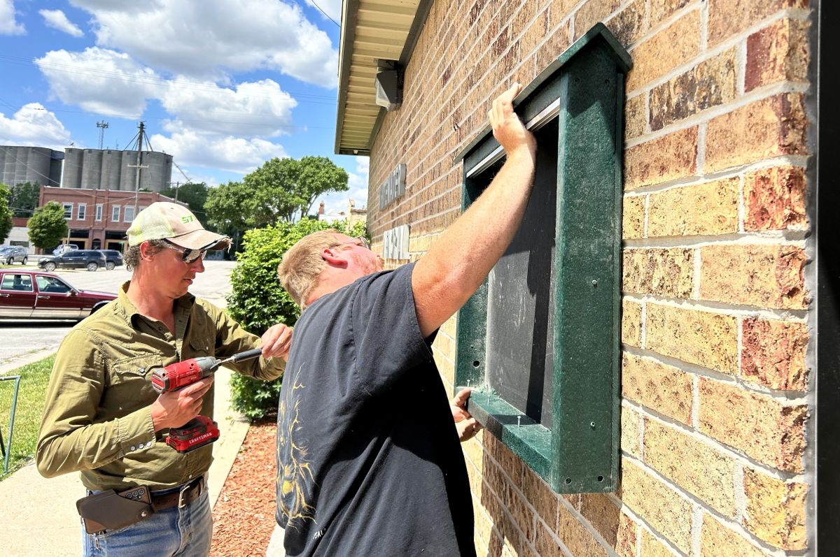 two city workers hanging an outdoor bulletin board